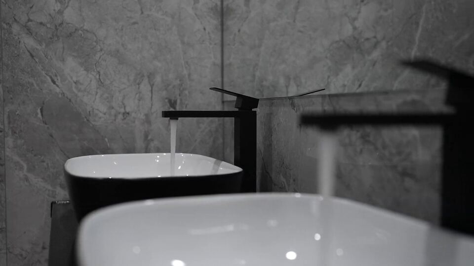 Water running from a black square mixer tap into a vessel basin