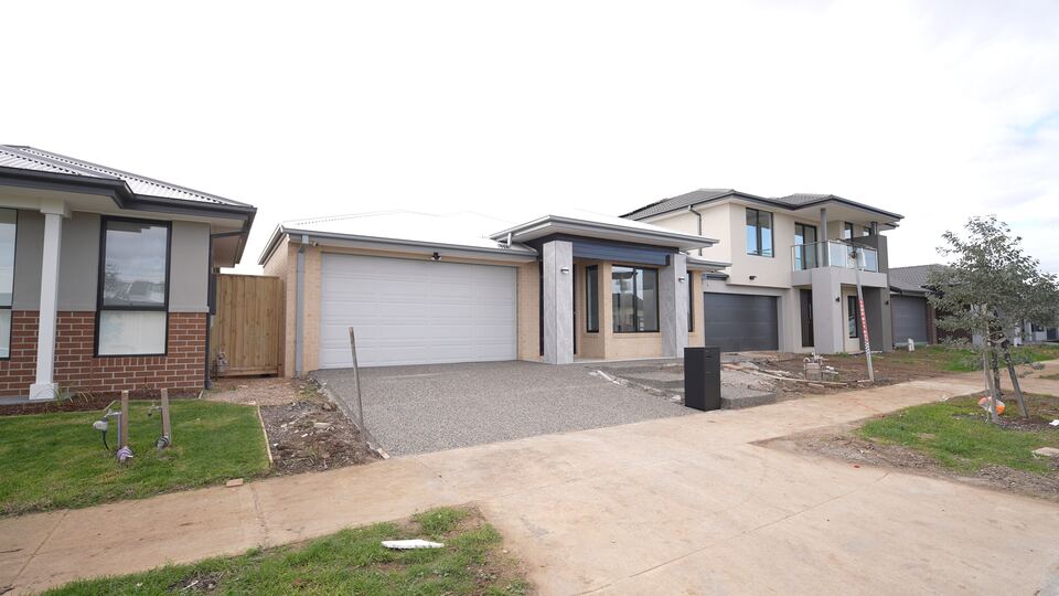 Front of our Jagged Circuit home: a single-storey home in cream brick with a white double garage door, grey stone-look entry pillars and an exposed-aggregate driveway