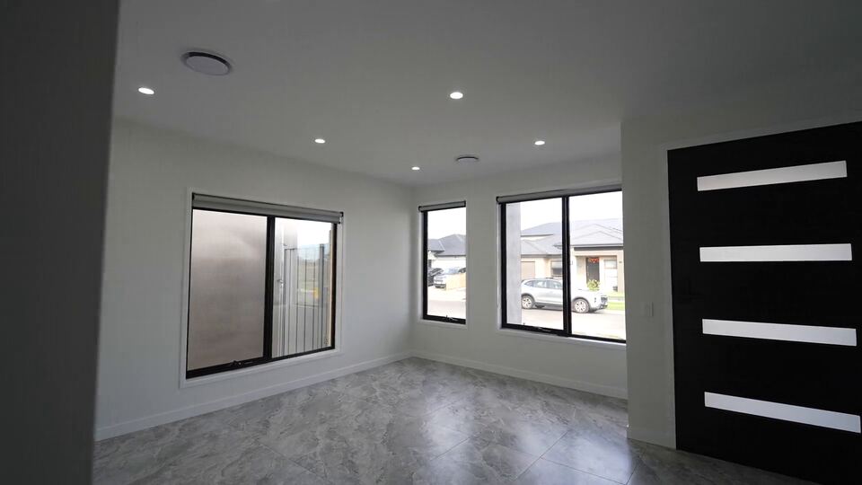 Front room with grey tiled floor, three windows and the black front door with frosted glass strips