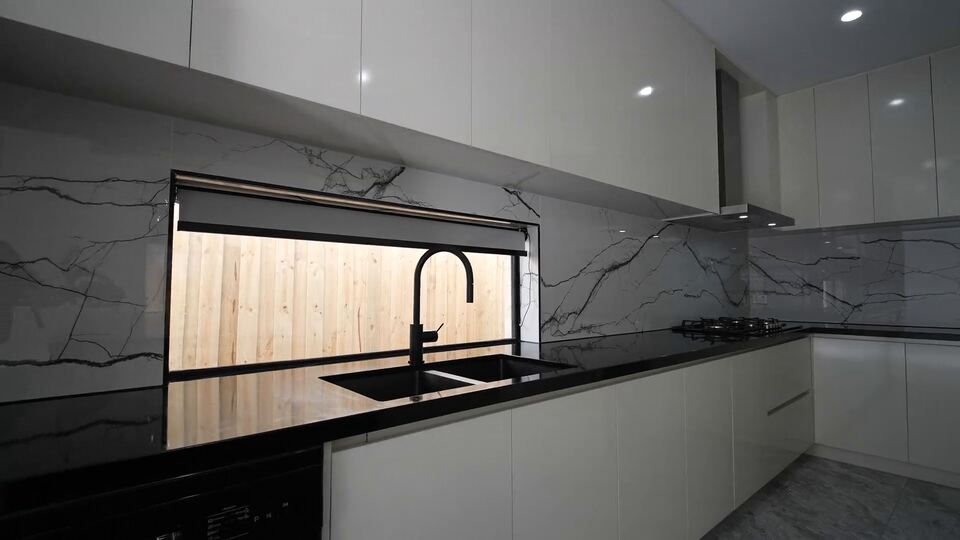 Kitchen with gloss white cabinets, black benchtops, a marble-look splashback and a window splashback behind the sink