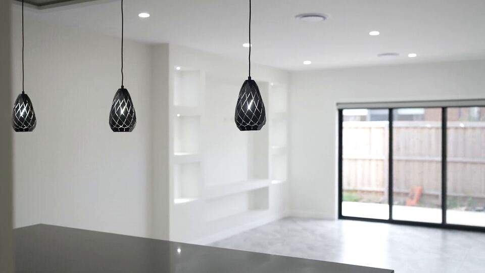 Open-plan living area with three black pendant lights over the kitchen island, built-in white shelving and sliding doors to the backyard