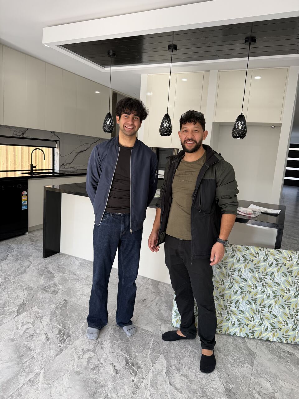 The homeowner and Yash Batish standing in the finished kitchen under three black pendant lights