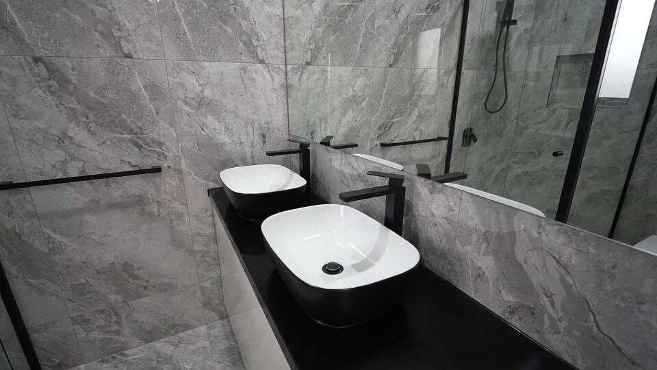 Double vanity with two black and white vessel basins, black mixer taps and grey marble-look wall tiles