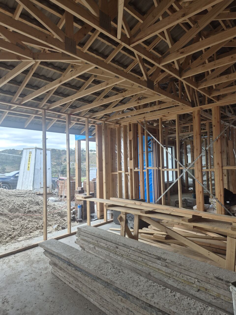 Garage and porch framing at Ladhams Way with roof trusses above and materials stacked inside