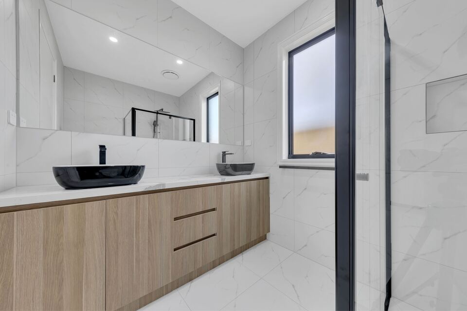 Bathroom at Lucania Crescent with a timber-look vanity, two black vessel basins and white marble-look tiles