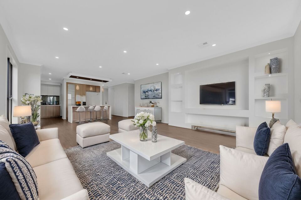 Open-plan living room at Lucania Crescent with timber-look floors, built-in shelving and the kitchen behind (furniture digitally added)